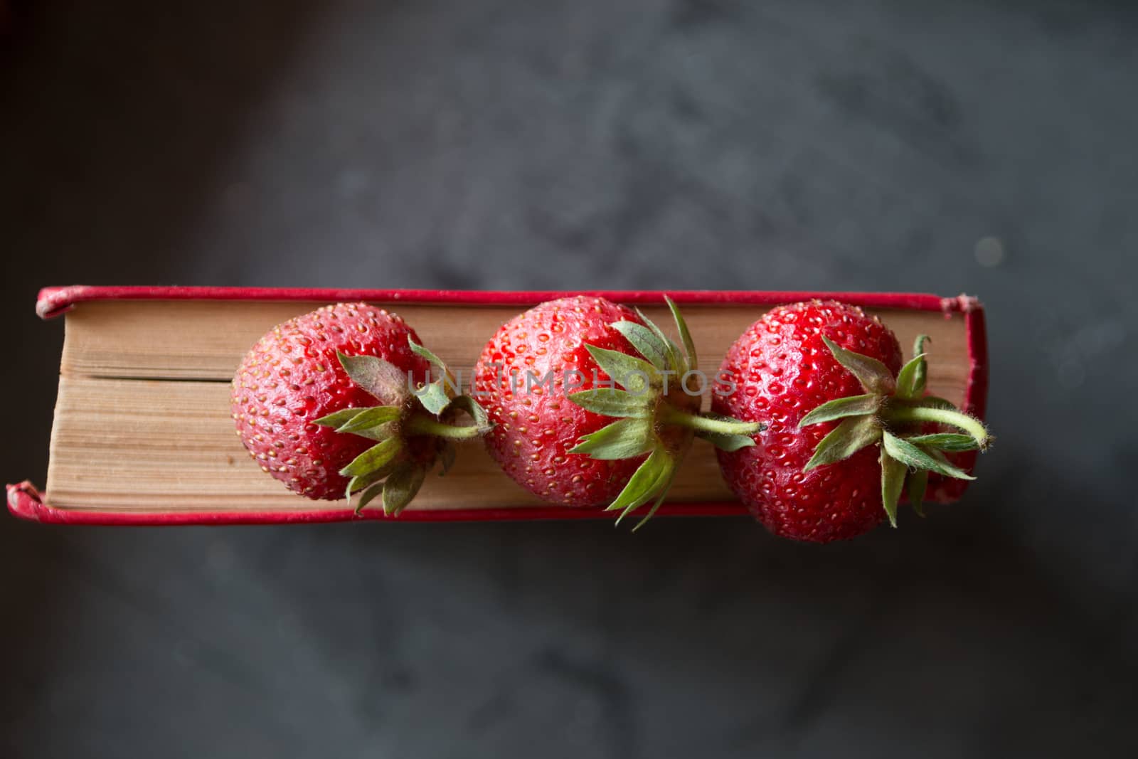 Strawberries and  red cook book on a dark table