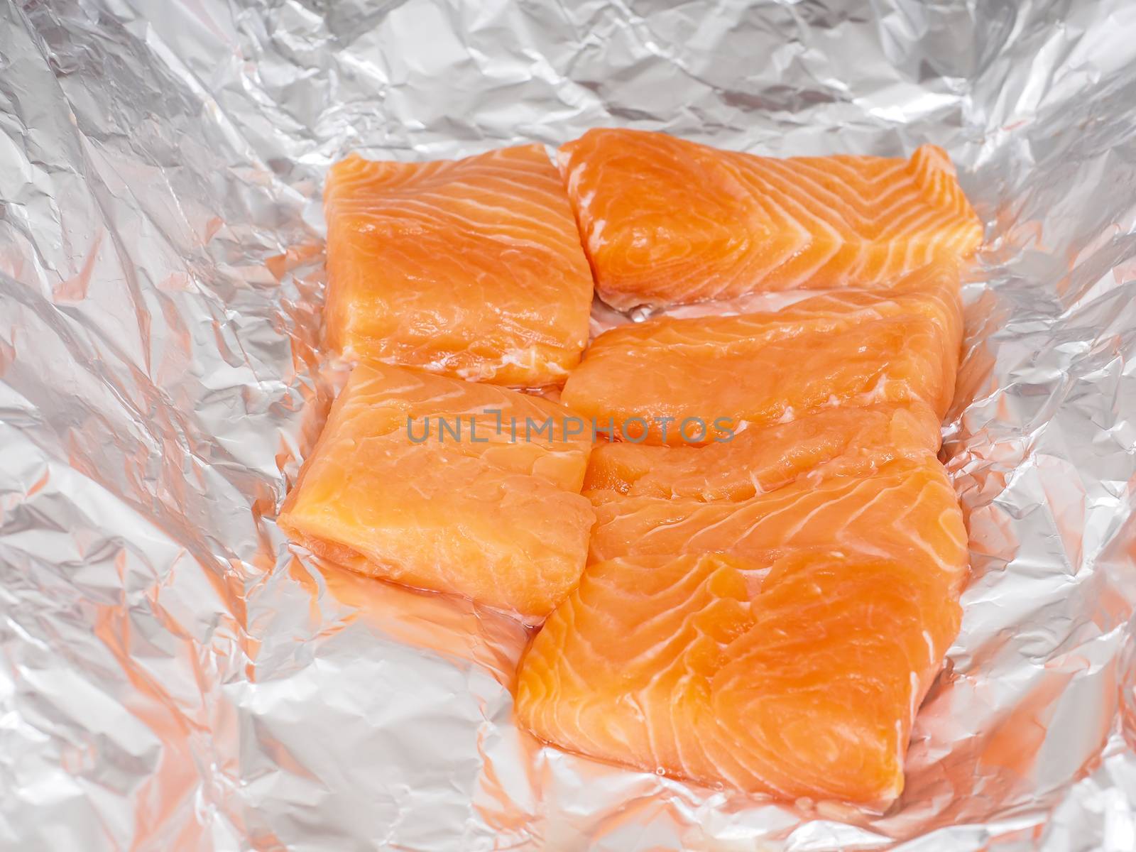 Closeup of unseasoned salmon pieces in aluminum foil by Arvebettum