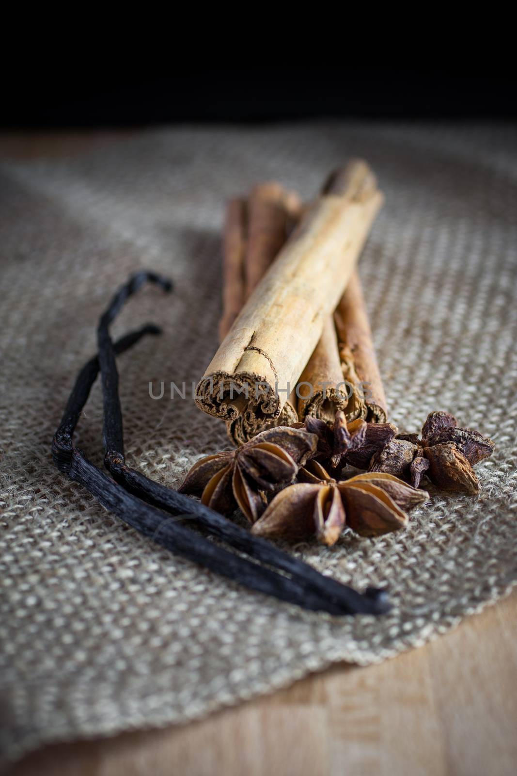 Fresh vanilla beans, cinnomon sticks, and star anise on a burlap surface and highlighted in the sun from a nearby window.