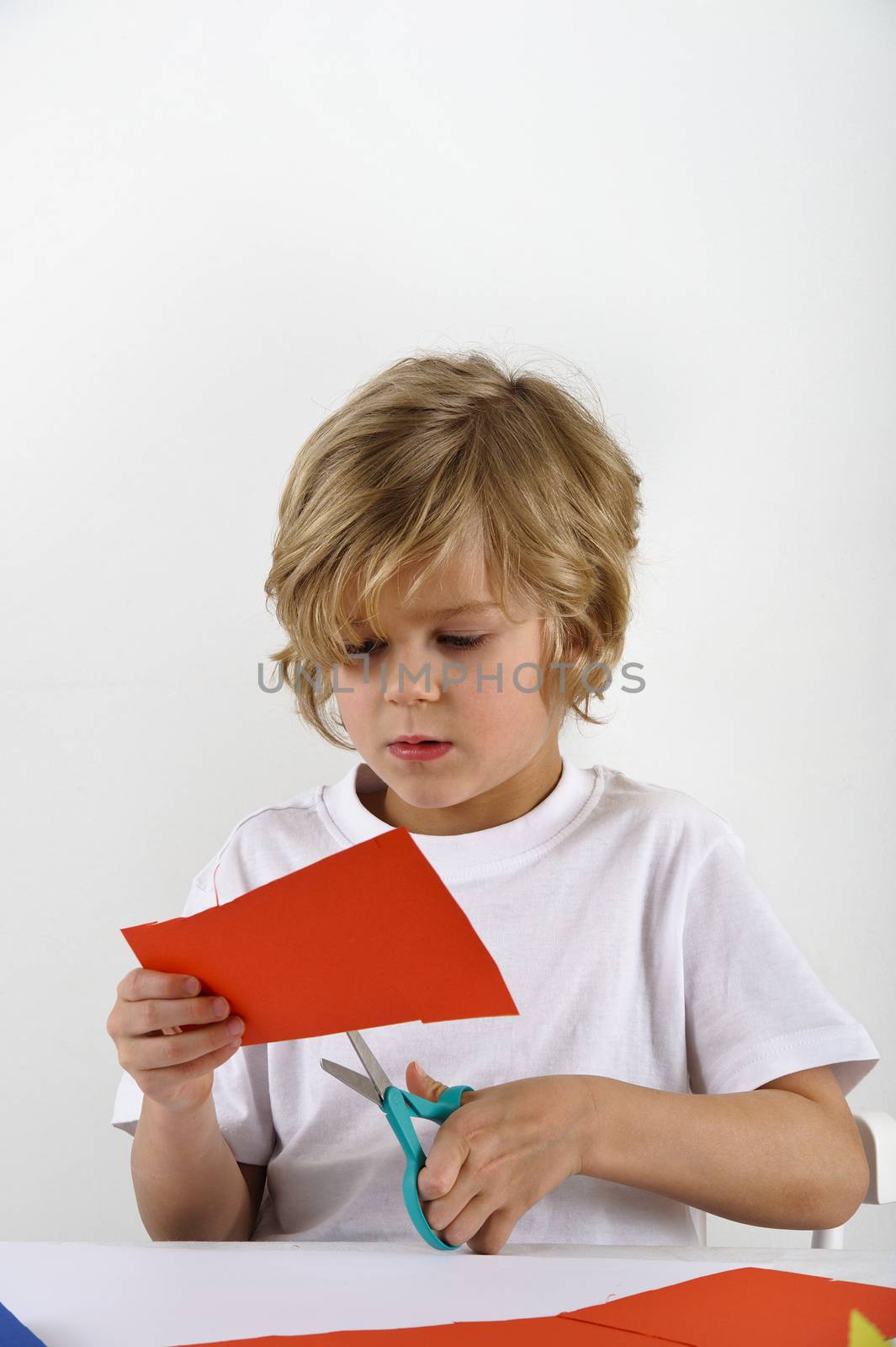 young boy cuts red colored paper with a scissors