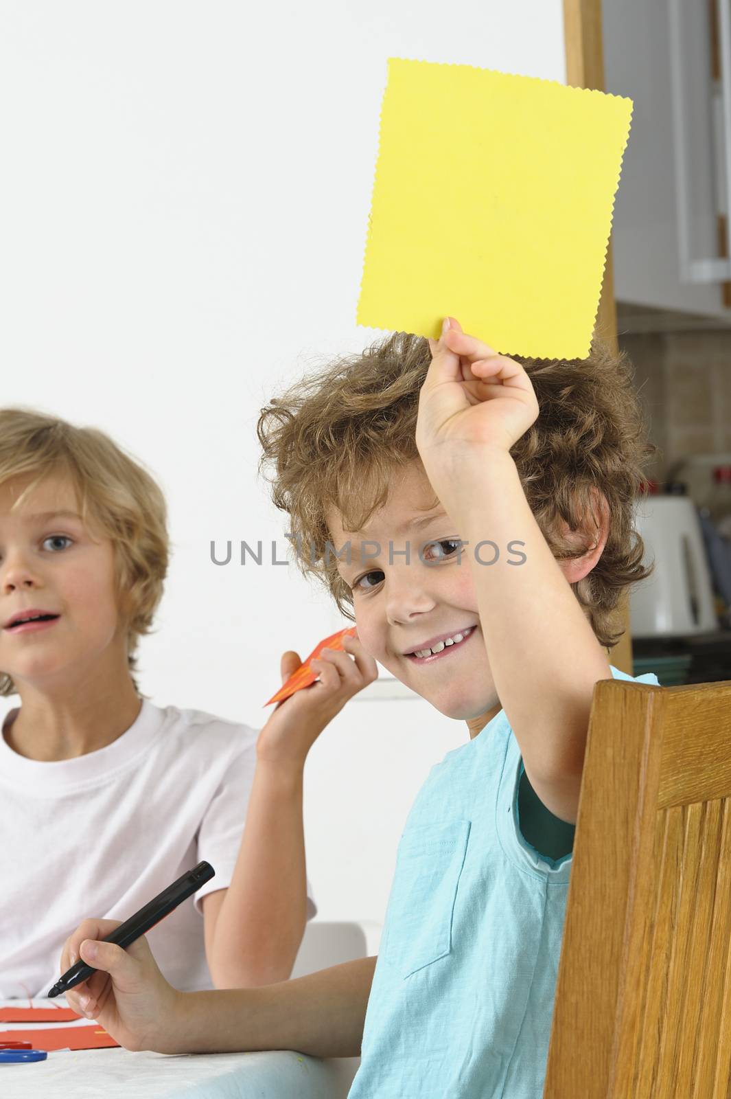 Young boy holds up a blank yellow card. Another boy in the background looks at the camera.
