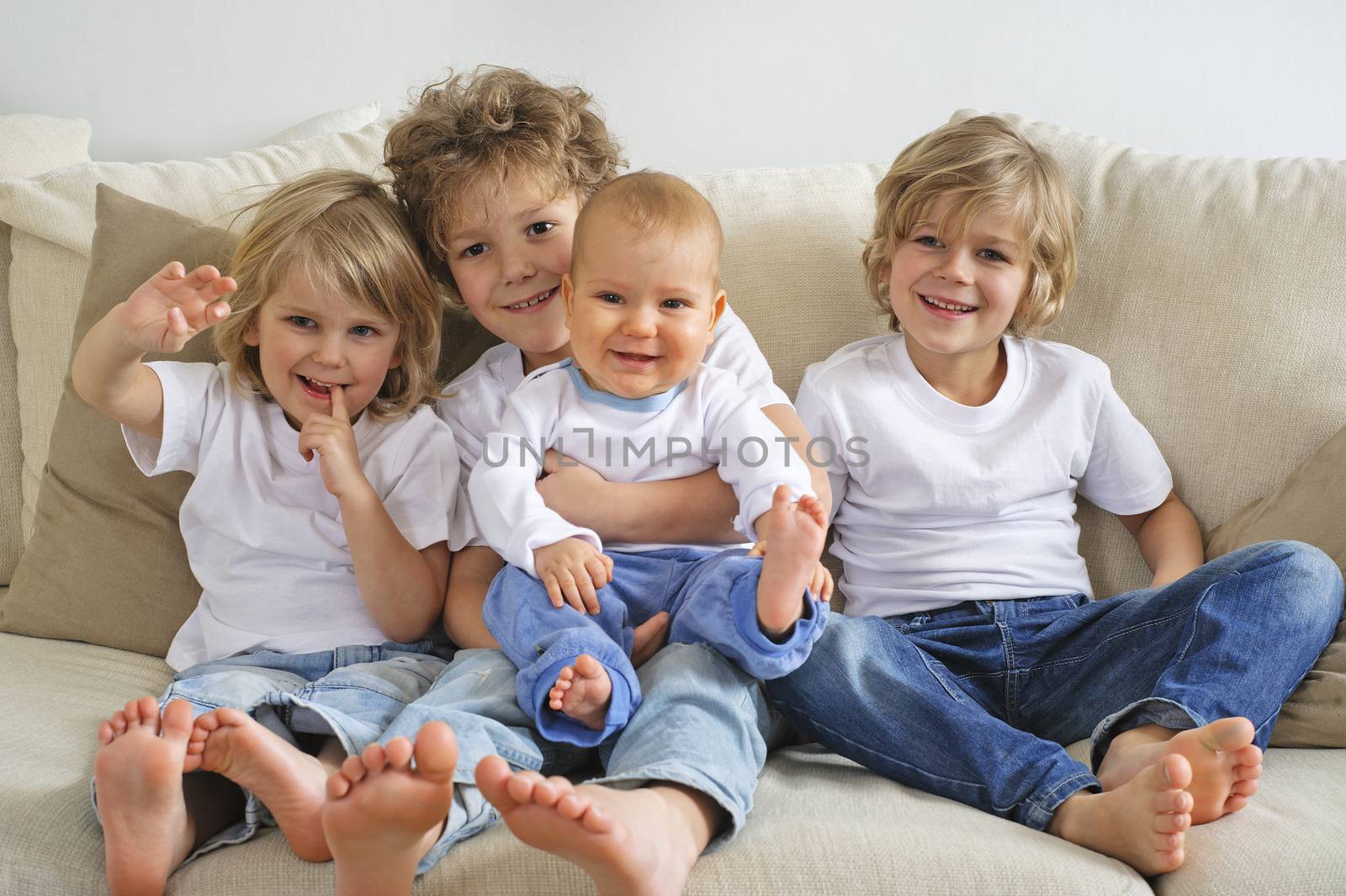 Four brothers, young boys, sitting on a sofa. The eldest is holding a baby in his lap. They're looking to the left of the camera