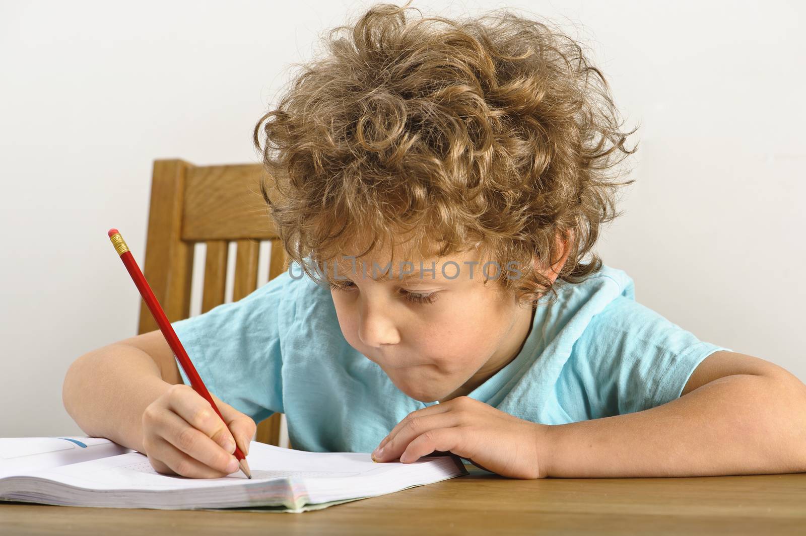 Curly haired young boy sits at a wooden table and does his homework