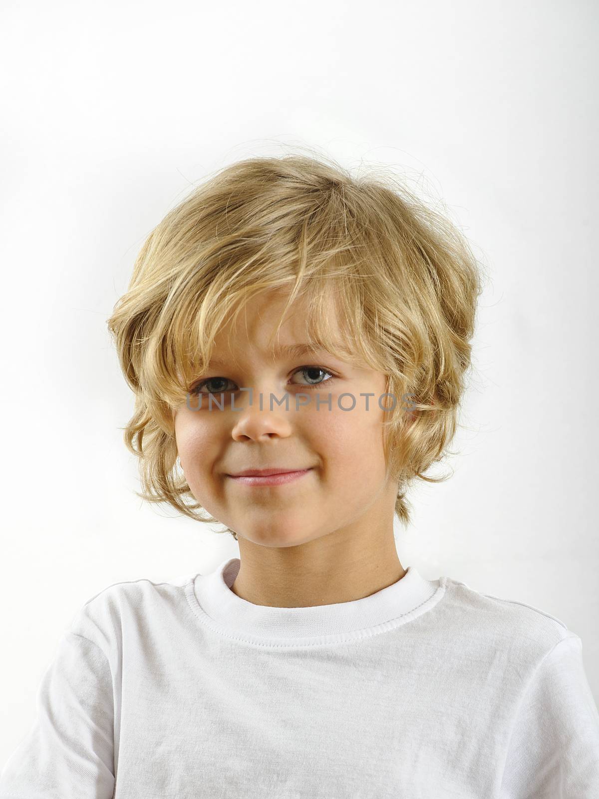 Young blond haired boy looking at camera. He's wearing a white shirt. Background is white