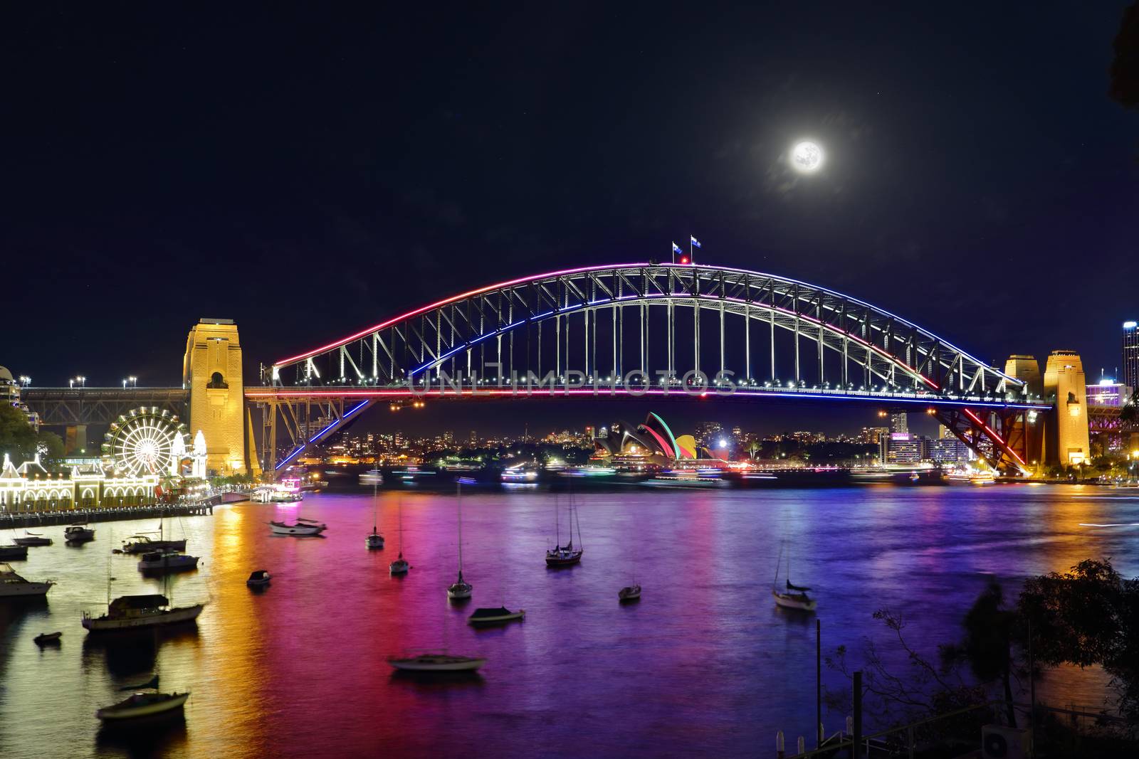 NTH SYDNEY, AUSTRALIA - JUNE 6, 2015;  Scenic views across Lavender Bay, Sydney Harbour to  Sydney Harbour Bridge and Sydney Opera House and city buildings during Vivid Sydney annual festival.  Reflections from coloured lights illuminate the harvour in a rainbow of colour.