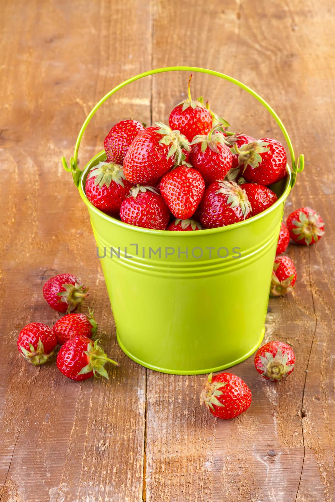 strawberry in a green metal bucket on wooden  by manaemedia