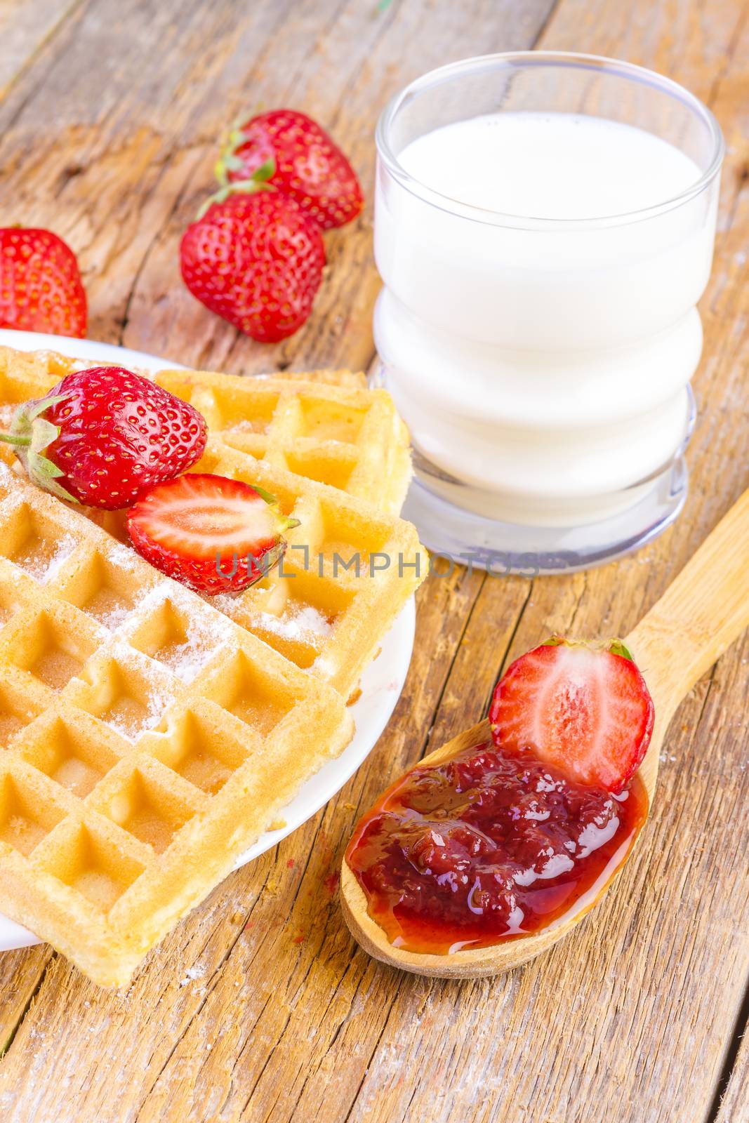 homemade waffles with strawberries maple syrup and glass with milk on wooden background