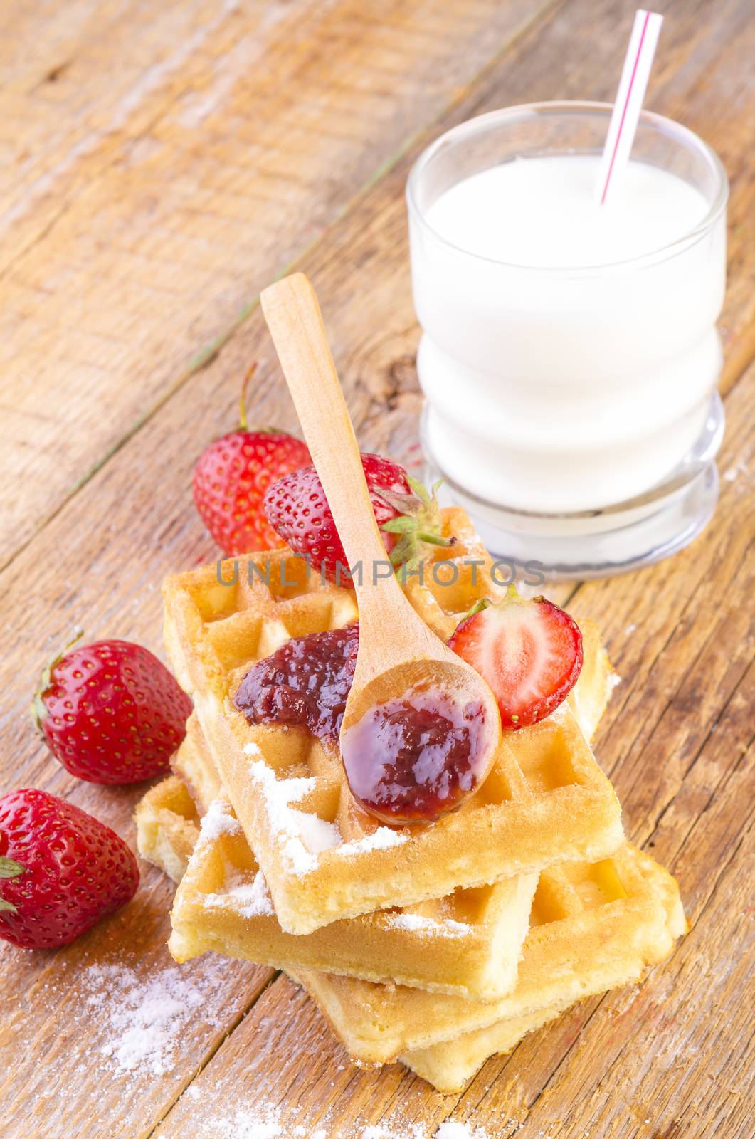 homemade waffles with strawberries maple syrup and glass with milk on wooden background