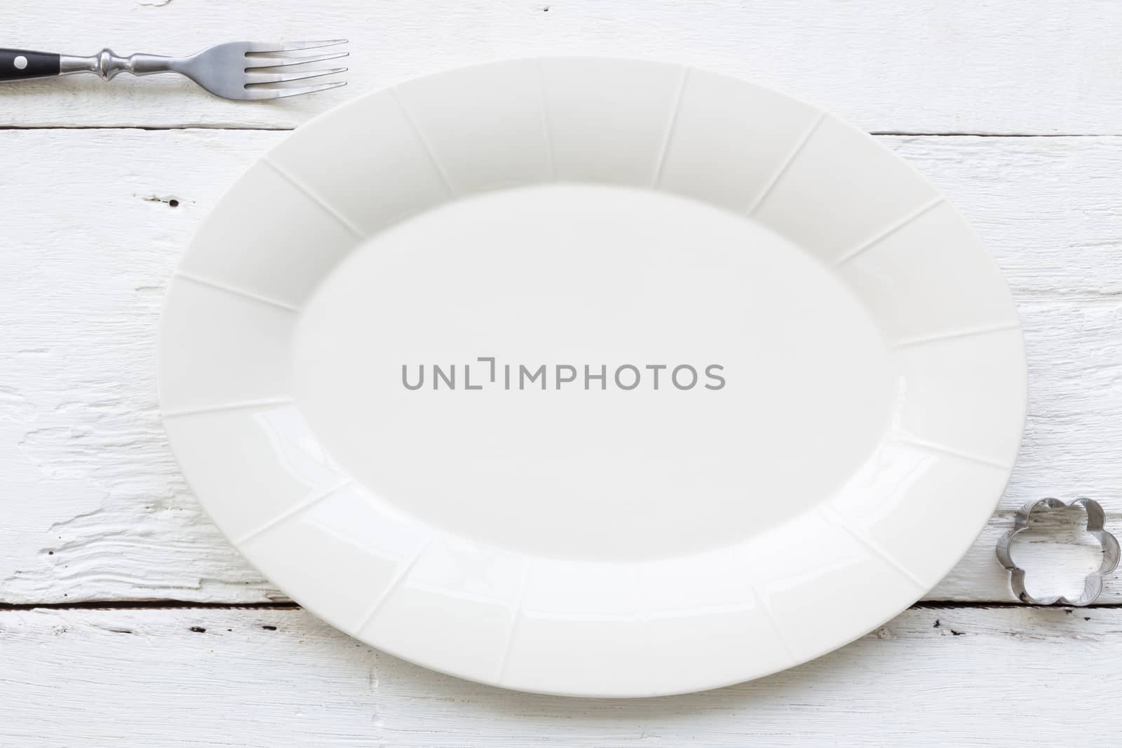 Top view of empty oval ceramic plate, fork and flower shape cookie cutter putting on white wooden table. retro, vintage and country style image