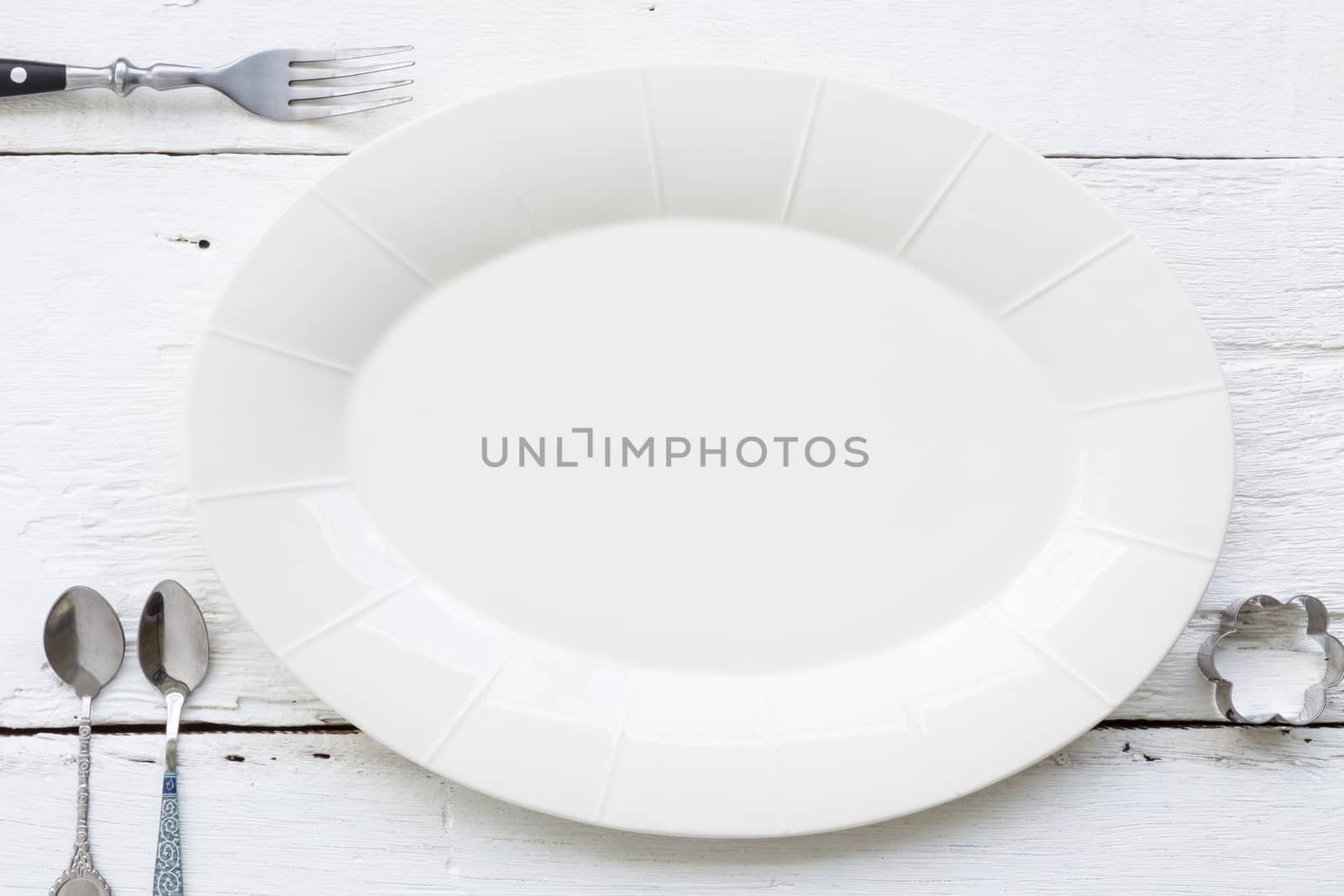 Top view of empty oval ceramic dish, fork, teaspoons and flower shape cookie cutter putting on white wooden table. retro, vintage and country style image