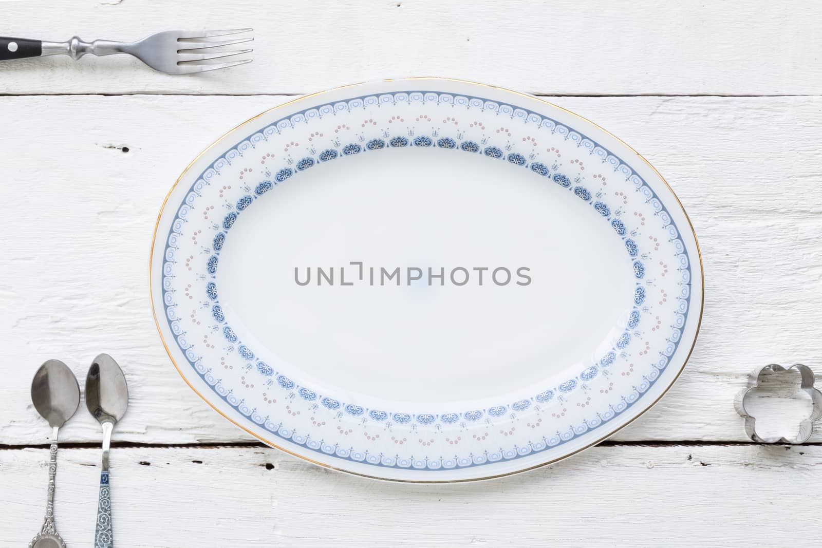 Top view of beautiful old dessert plate, fork, teaspoons and flower shape cookie cutter putting on white wooden table. retro and vintage style image