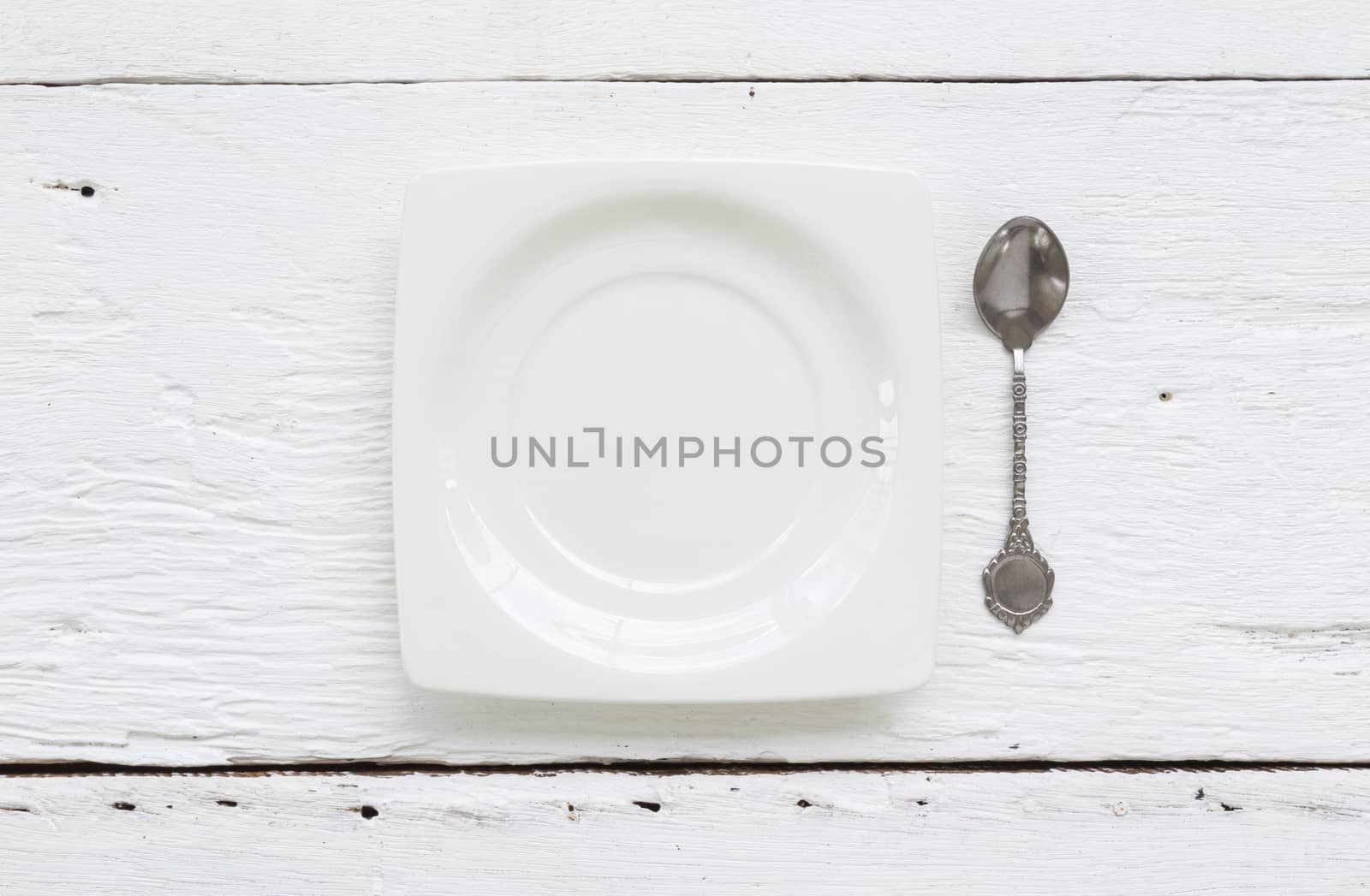 Top view of white ceramic square dessert plate and vintage teaspoon putting on old wooden table.