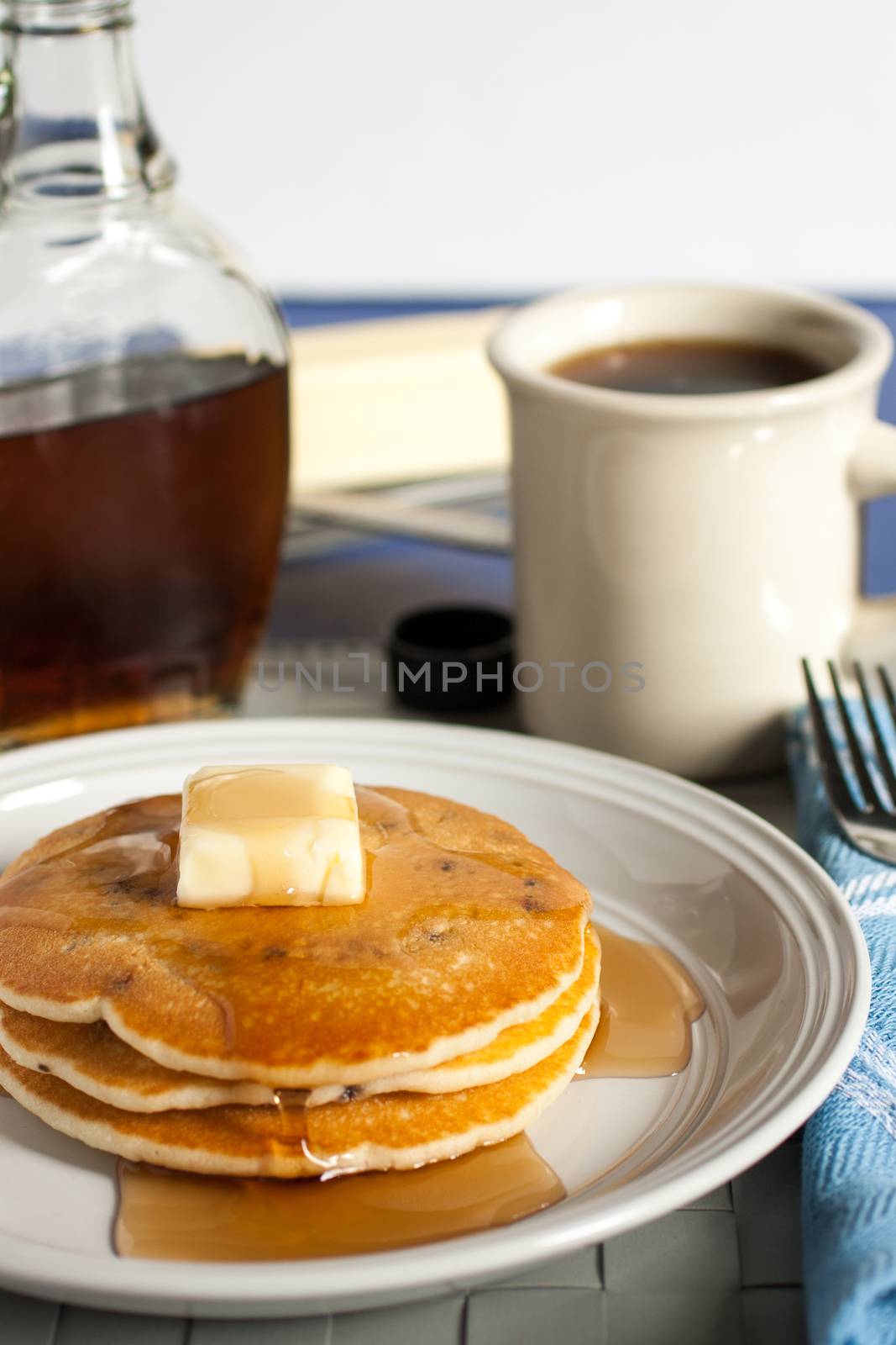 Fresh pancakes on a white plate with maple syrup, butter and a cup of coffee.