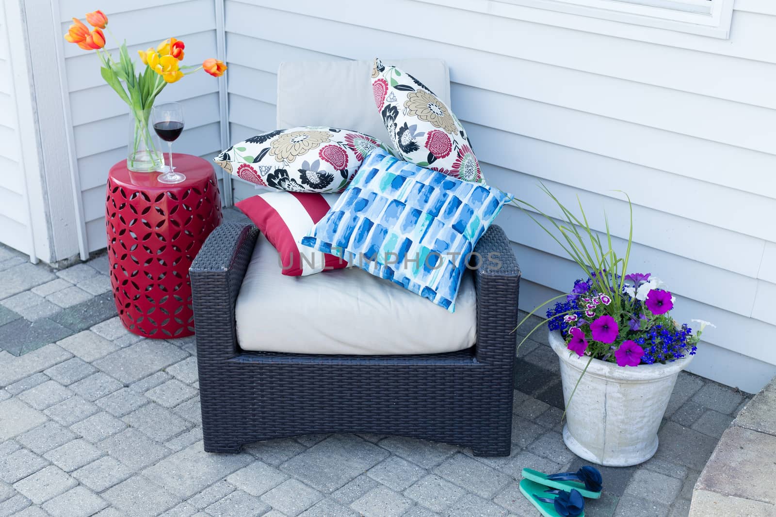 Pile of colorful cushions on a comfortable outdoor armchair flanked with fresh spring tulips and flowers for a relaxing place to enjoy a shady break on a hot day