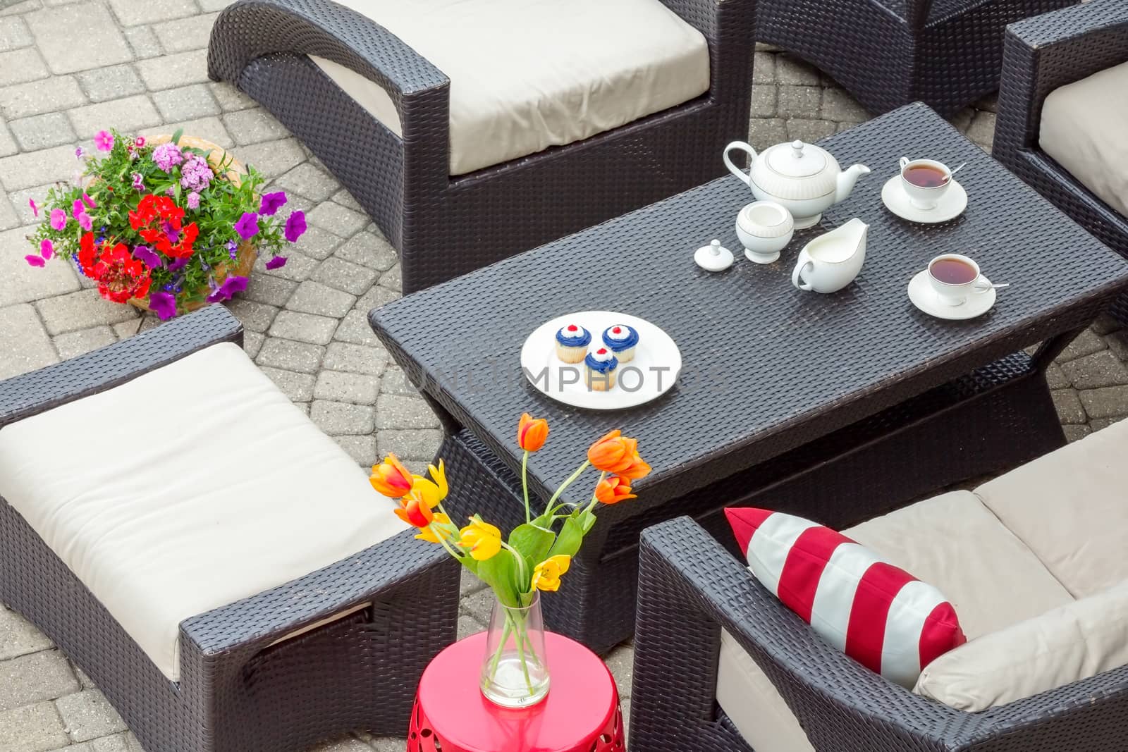 4th July tea served on an outdoor patio with patriotic cupcakes and cups of tea on a table surrounded by comfortable armchairs and a stool with spring tulips in a vase