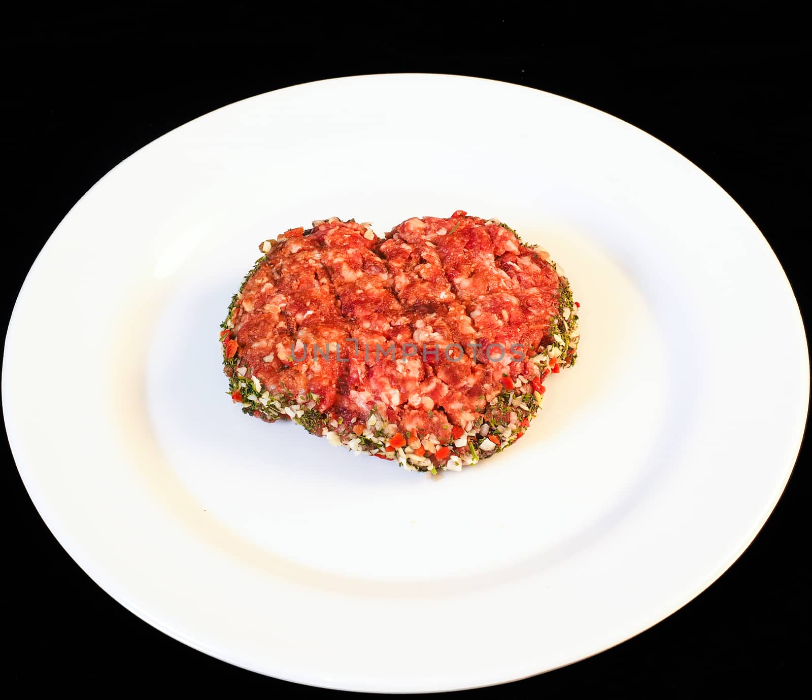 Seasoned raw red hamburger on white plate isolated on black by Arvebettum