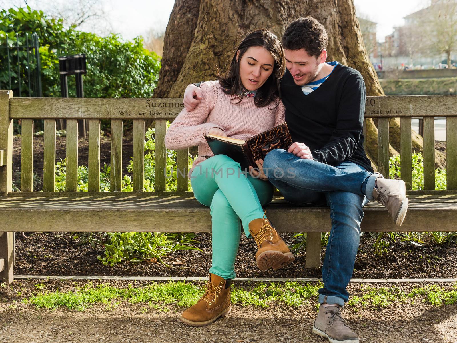 Young Couple Sitting on a Bench Reading a Book by PhotoLondonUK