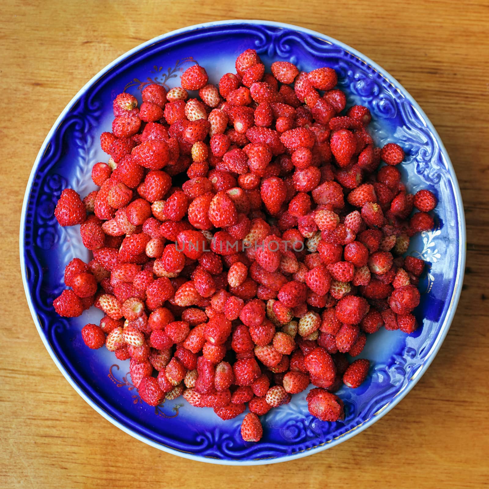 Fresh ripe wild strawberries in a bowl on wooden table