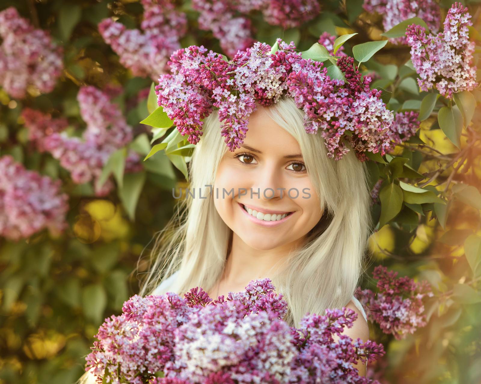 Beautiful smiling young woman is wearing wreath and bouquet of lilac flowers 