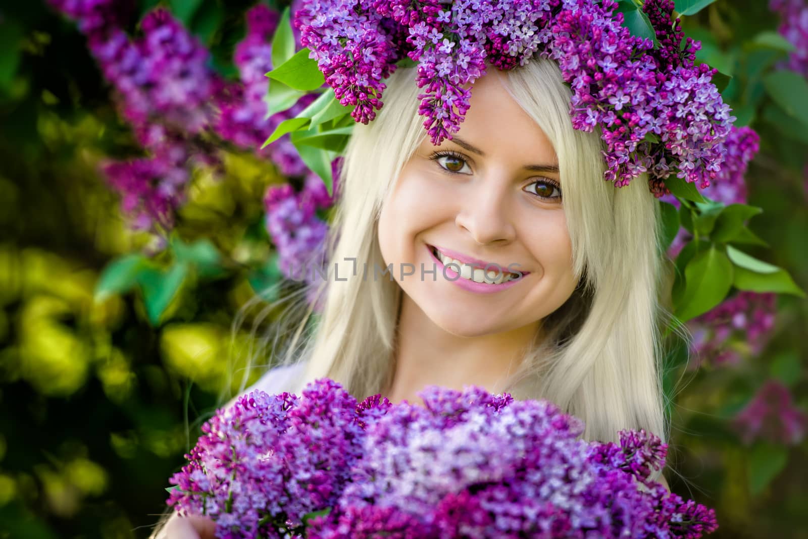 Close Up portrait beautiful smiling young blonde woman is wearing wreath of lilac flowers and bouquet
