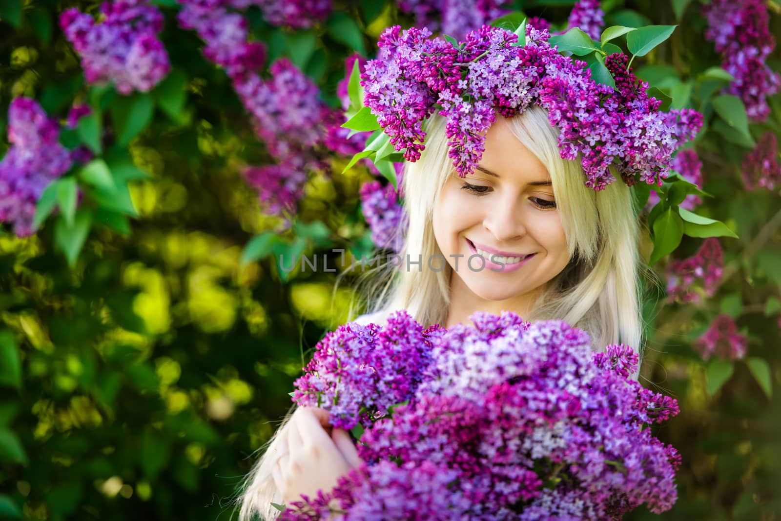 Beautiful smiling young woman is wearing wreath and bouquet of lilac flowers 