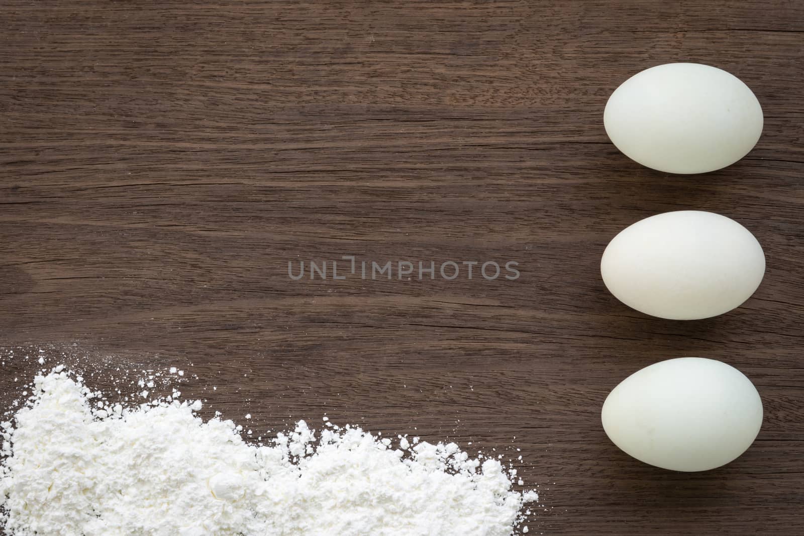 Top view of cooking background with three eggs and flour on vintage natural wood table. Rough texture and rustic surface with free text space.