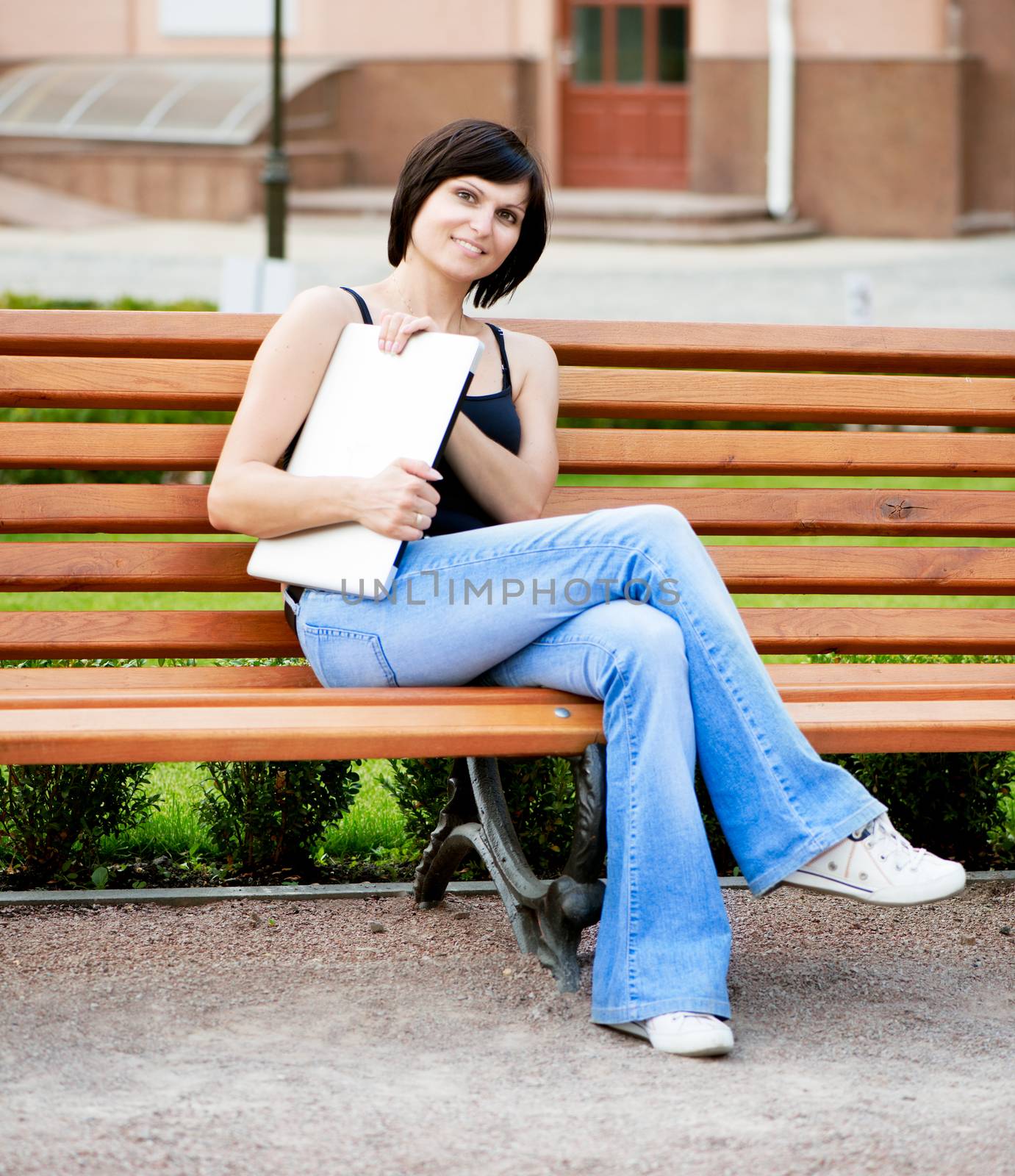 Young brunette girl sitting on a sunny day on a bench in the park with laptop in her hands