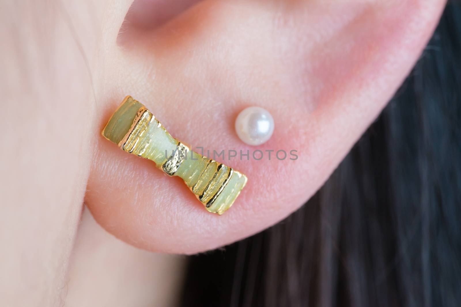 A macro shot of a green ribbon earring and white pearl earring in a girl's ear.