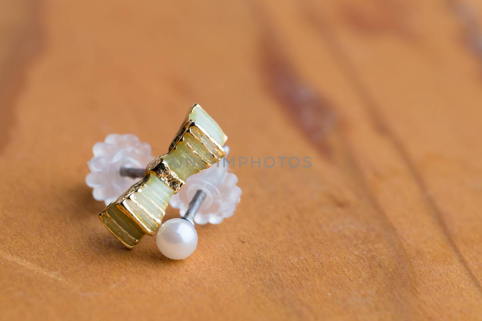 A macro shot of a green ribbon earring and white pearl earring.