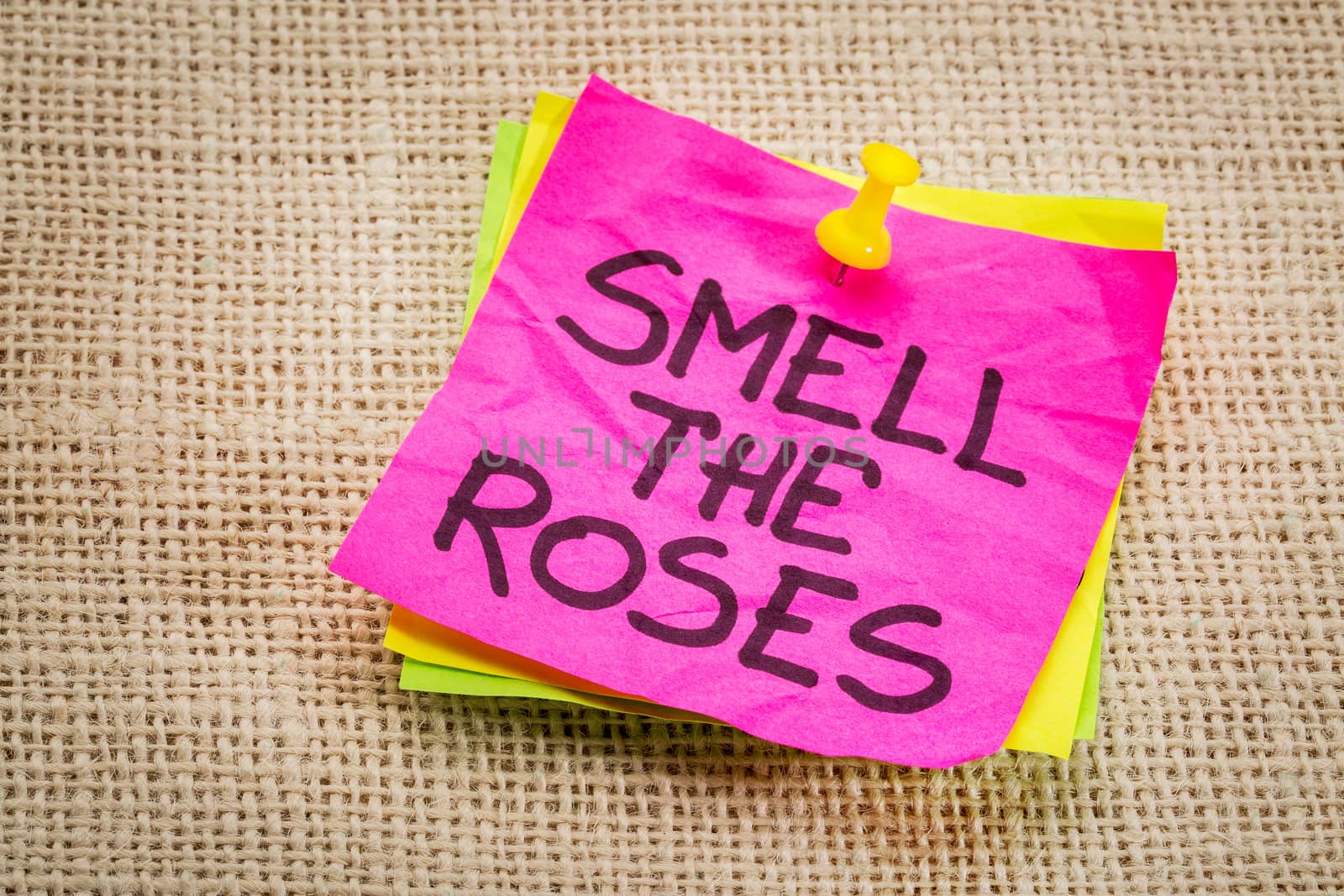 smell the roses - inspirational reminder on a sticky note against burlap canvas