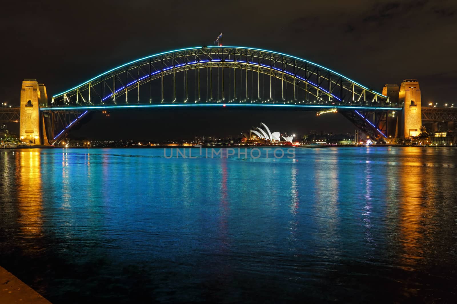 SYDNEY, AUSTRALIA - JUNE 3, 2013;  Sydney Harbour Bridge lit in blue and aqua colours and reflections in Sydney Harbour.  Sydney Opera House in far view.