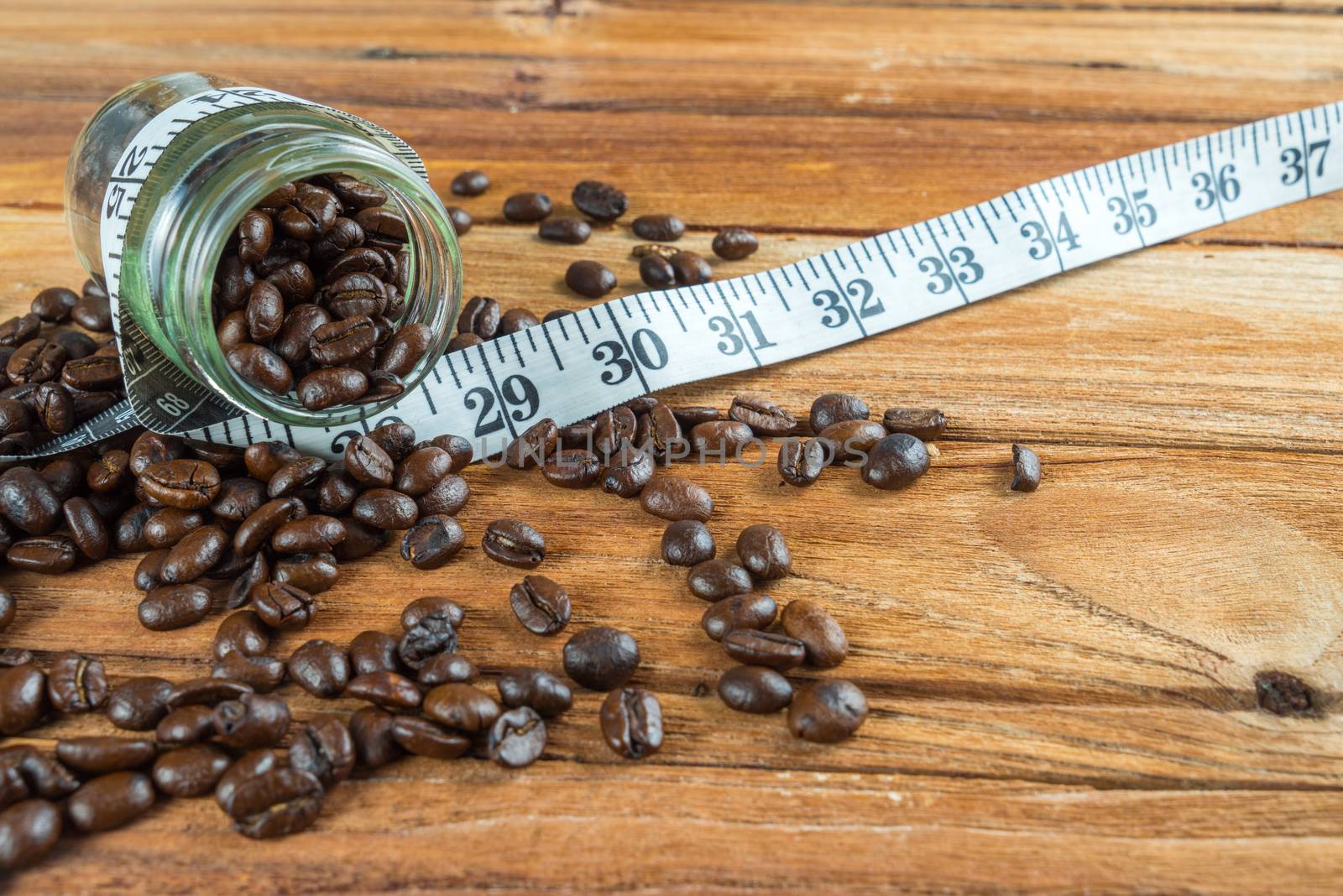 Coffee bean in glass bottle with tape measure on wooden table background