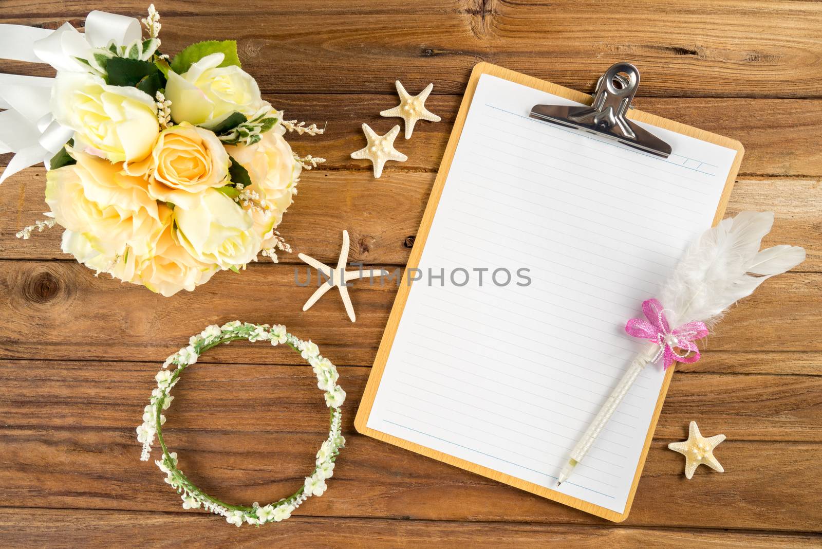 Wooden Clipboard attach planning paper with pen on top beside rose headband, tiara, bouquet, starfish