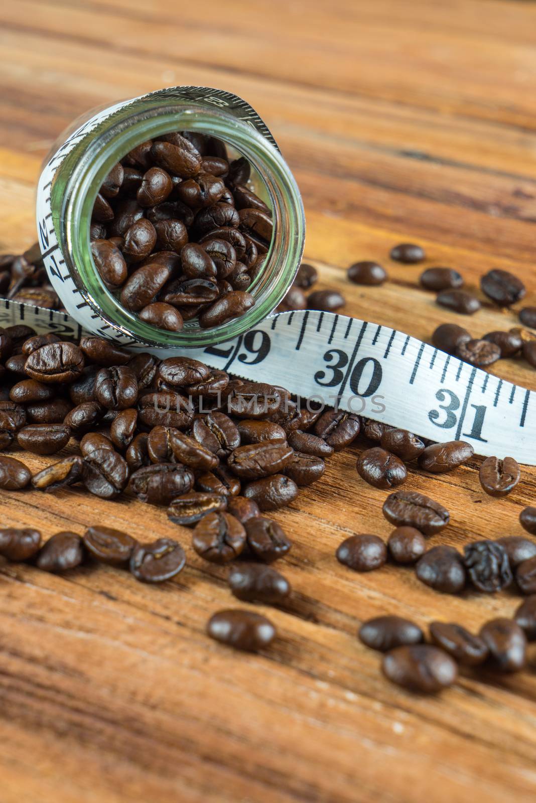 Coffee bean in glass bottle with tape measure on wooden table background