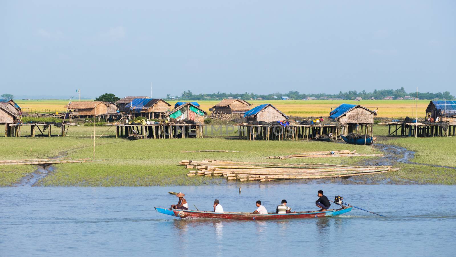 Sittwe, Rakhine State, Myanmar - October 16, 2014: Traditional boat passing a village along the Kaladan River at the Rakhine State in Myanmar.