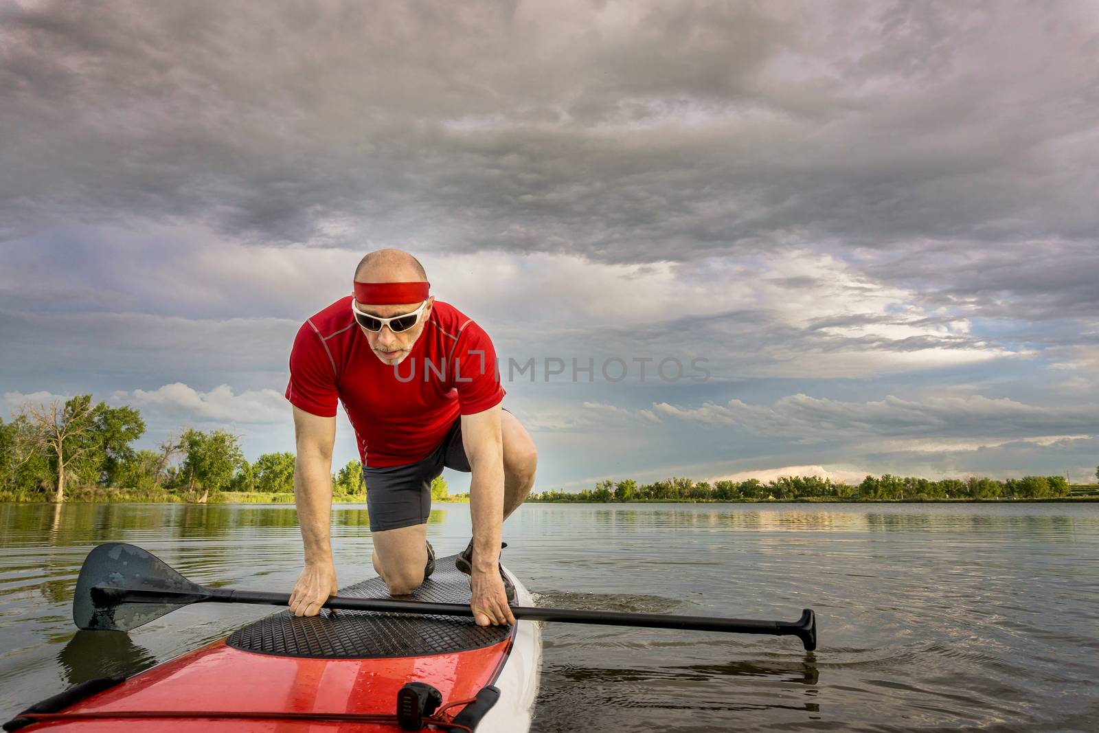senior male paddler starting his workout on  stand up paddleboard, a local lake in Colorado under cloudy sky