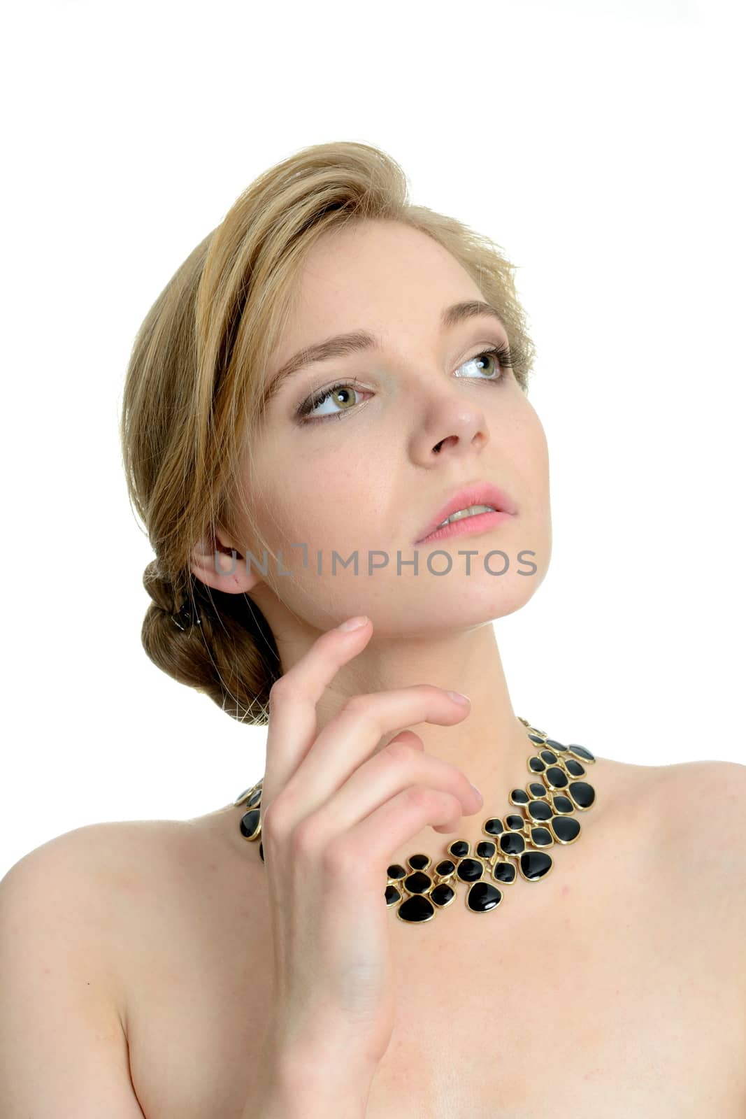 Portrait of young girl with blond hair and necklace. Female model holding hand near her chin.