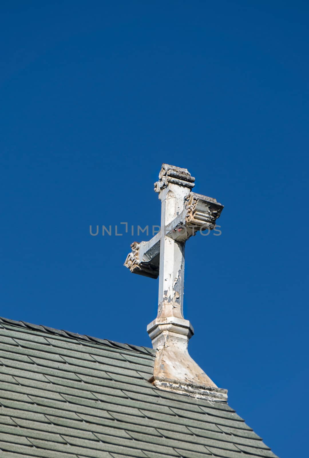 Ornate worn and peeling church cross against blue sky.