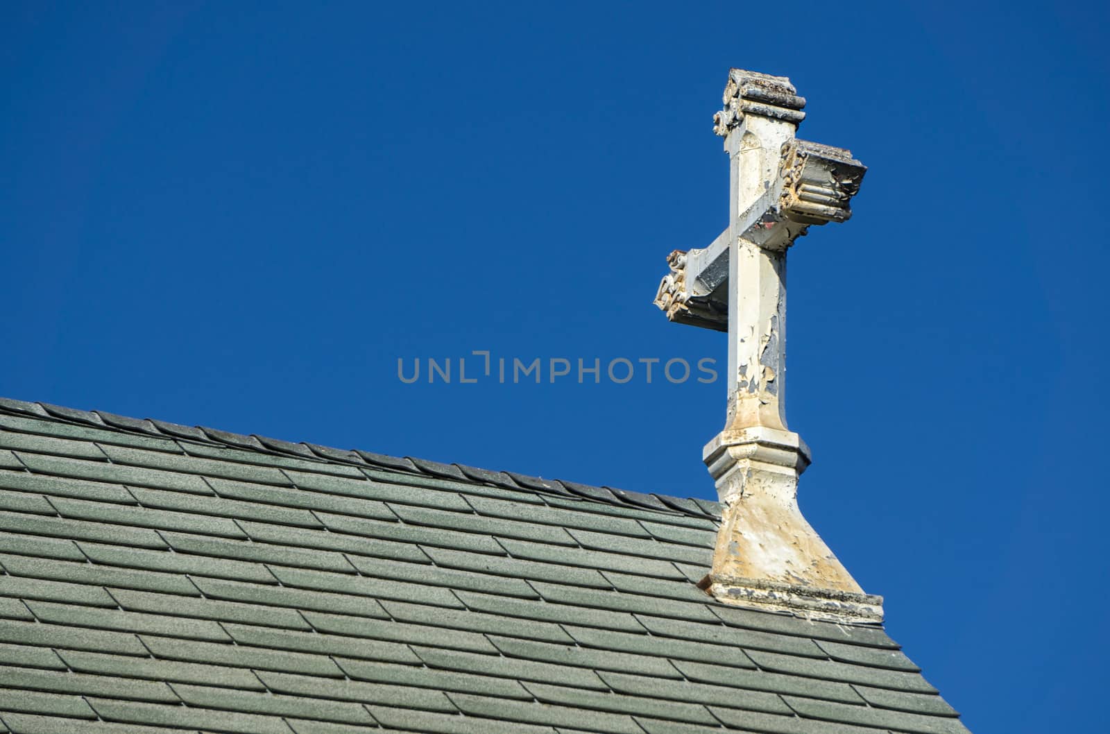 Ornate worn and peeling church cross against blue sky.