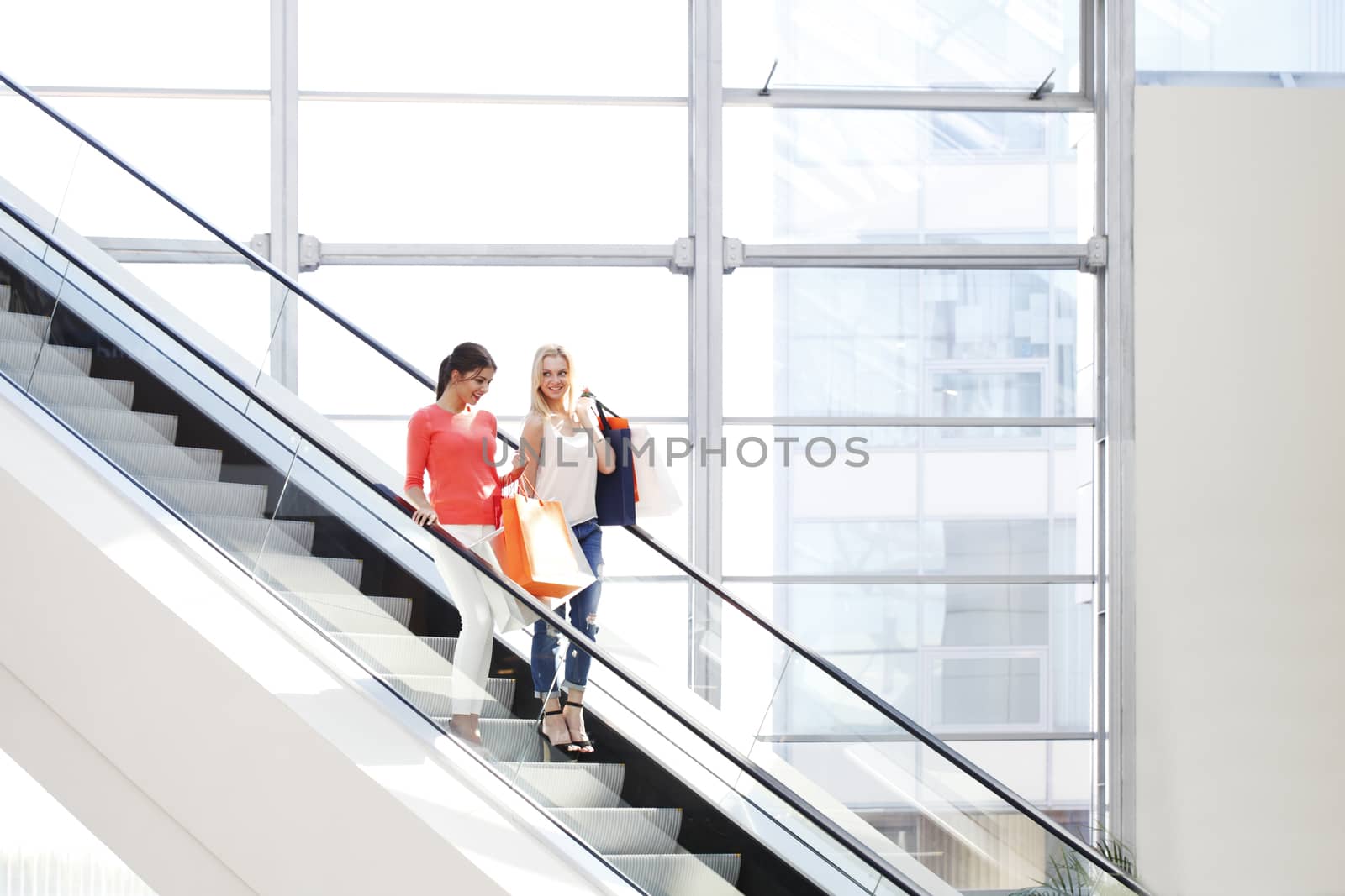 Young beautiful happy women on escalator of shopping mall