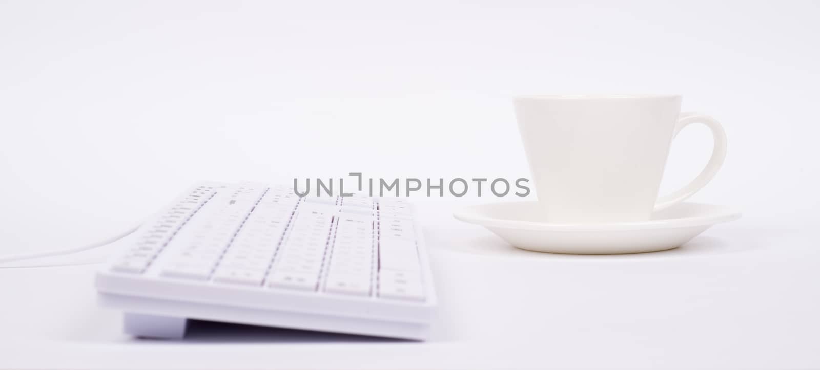 Computer keyboard and cup on isolated white background, side view