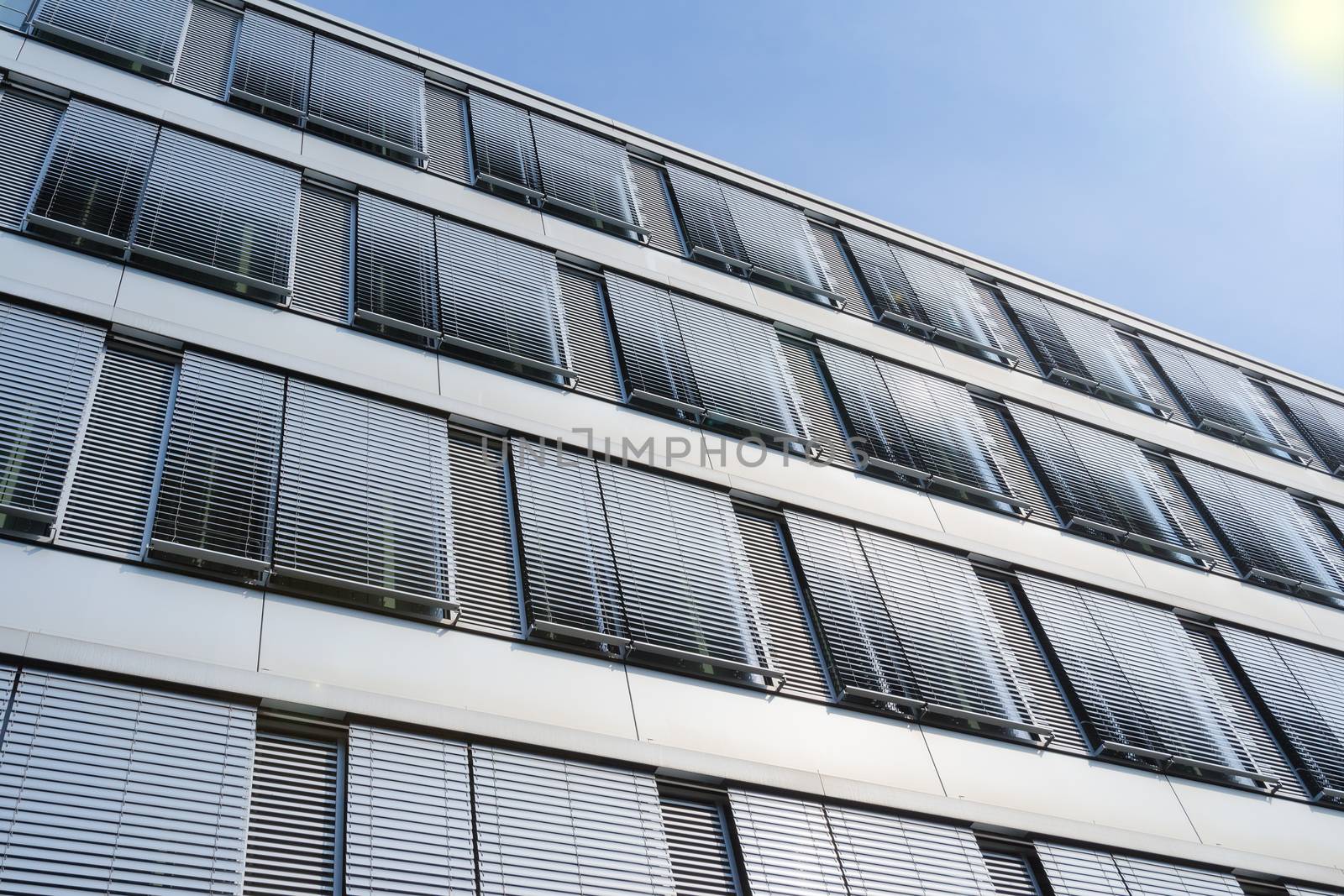 Facade of modern high-rise office building with covered windows Venetian blinds against blue sky