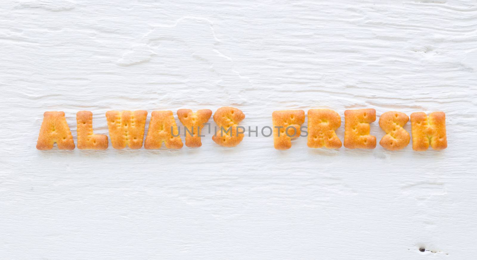 The capital letters word ALWAYS FRESH . Alphabet cookie biscuits putting on rough texture of white wood background.