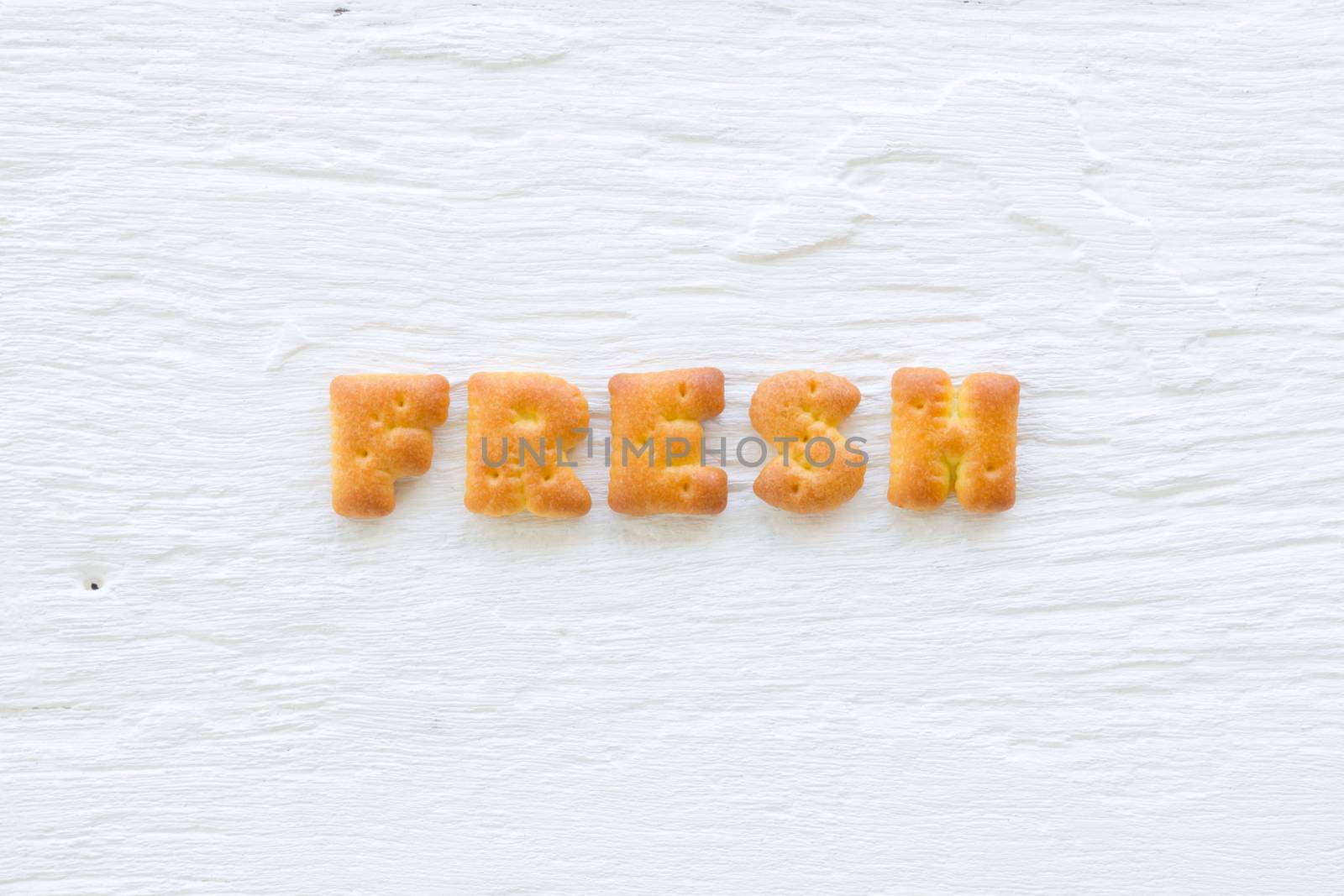 The upper-case letters word FRESH. Alphabet cookie crackers putting on rough texture of white wood background.