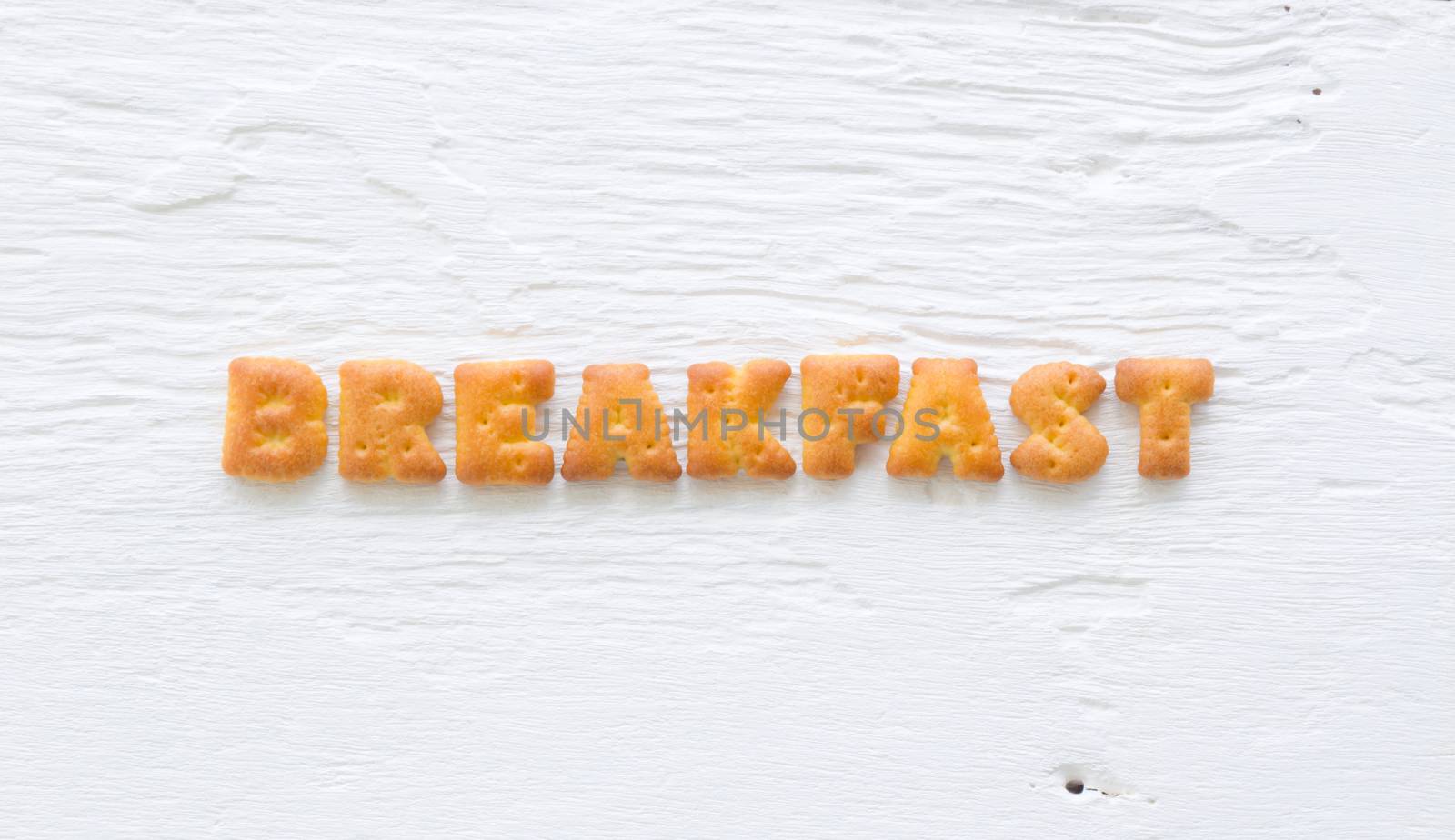 The character word BREAKFAST. Alphabet biscuit crackers putting on rough surface of white wood background.