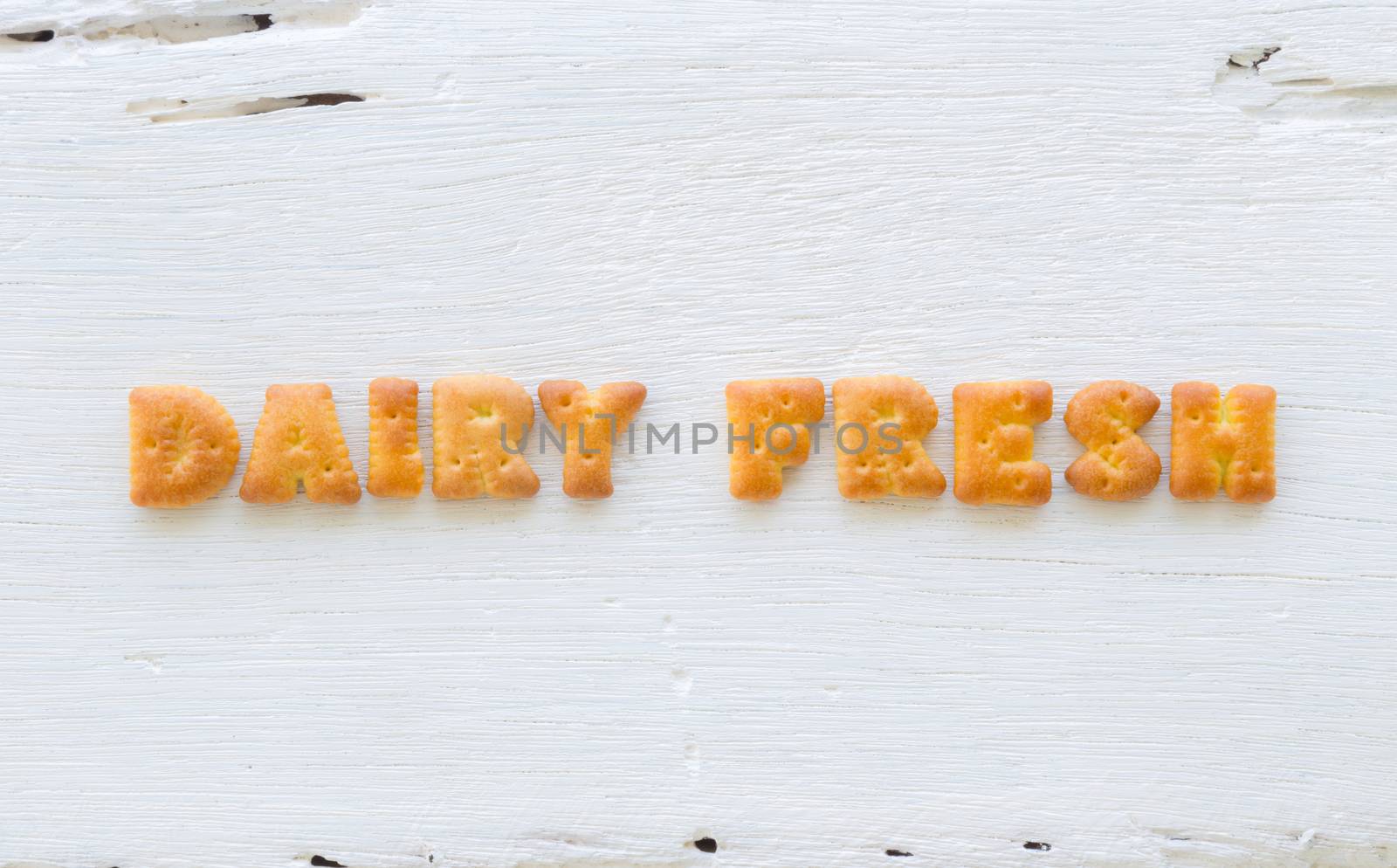 The character word DAIRY FRESH. Alphabet cookie crackers putting on rough surface of white wood background.