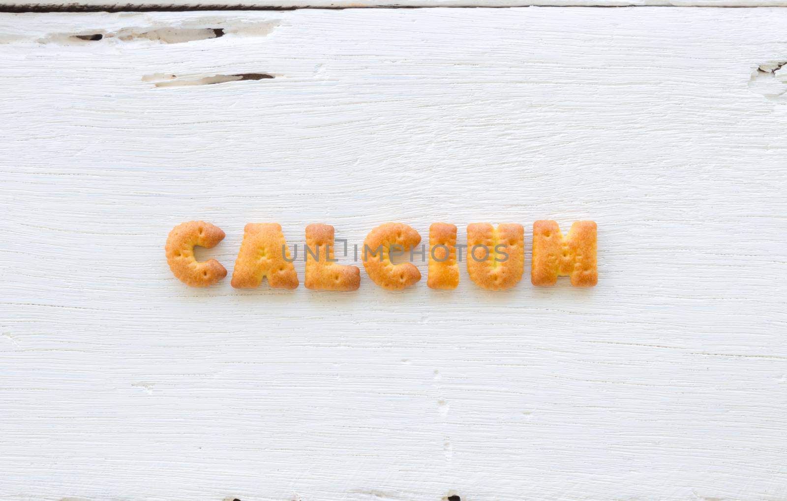 The upper-case letters word CALCIUM. Alphabet cookie crackers putting on rough texture of white wood background.