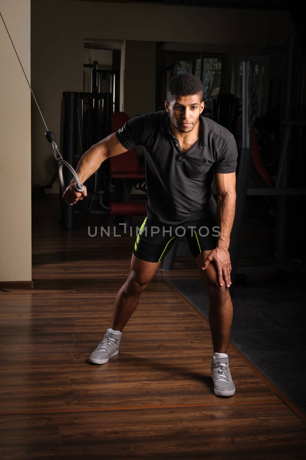 Handsome young african descent mixed race man doing one arm standing high cable fly workout in gym