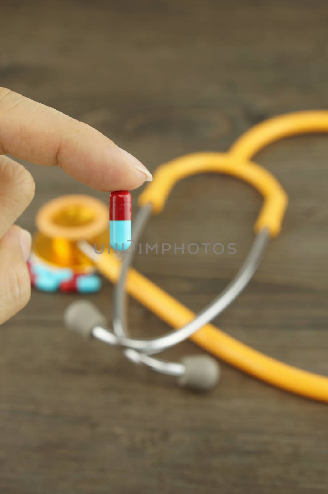 Doctor hold capsule in hand, stethoscope placed on desk.
                               