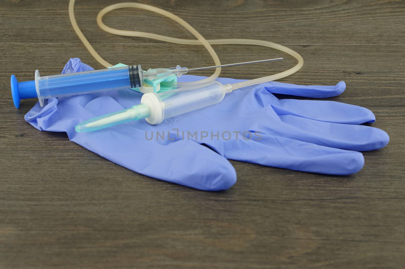 Disposable infusion set, syringe and glove placed on wooden table.
                              